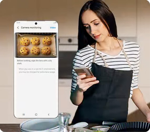 Frau mit Backschürze blickt auf Handy mit Back-App
