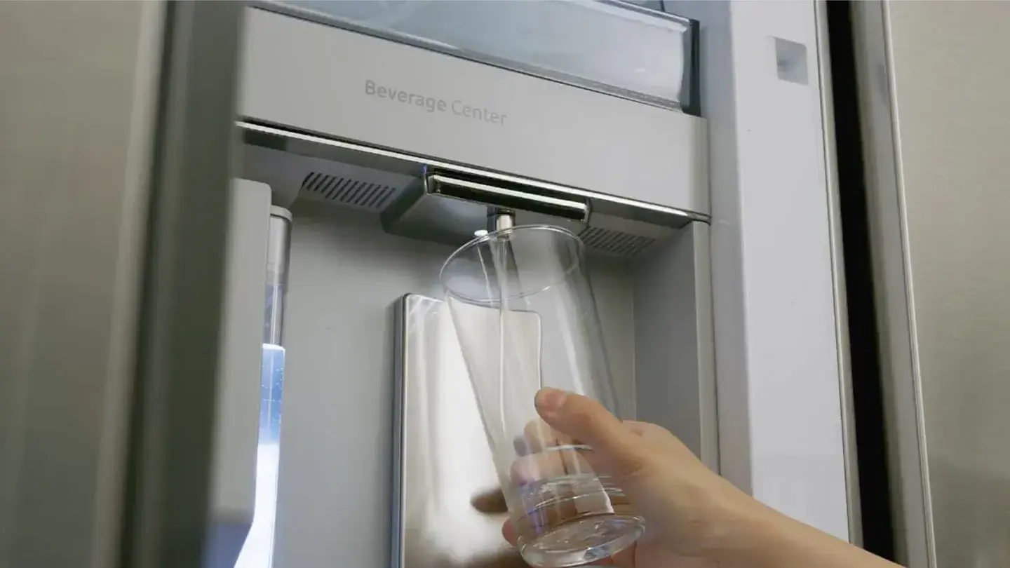 Hand mit Glas unter in Kühlschrank integrierten Wasserspender